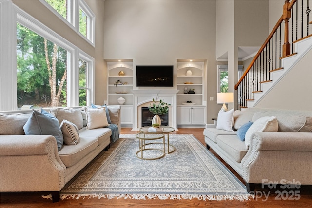 living area featuring a fireplace with flush hearth, a high ceiling, wood finished floors, and stairs