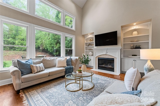 living room with a high ceiling, wood finished floors, built in features, and a wealth of natural light