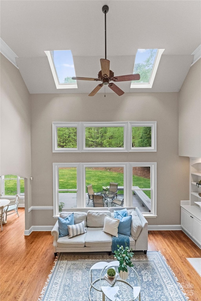 living area with high vaulted ceiling, ceiling fan, light wood-style floors, and a skylight