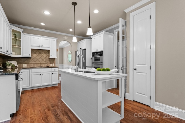 kitchen with white cabinets, an island with sink, ornamental molding, a sink, and dark wood-type flooring