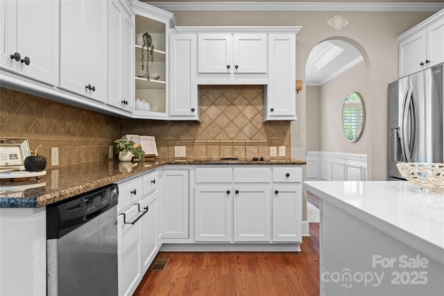 kitchen with white cabinets, dark wood-style floors, arched walkways, crown molding, and appliances with stainless steel finishes