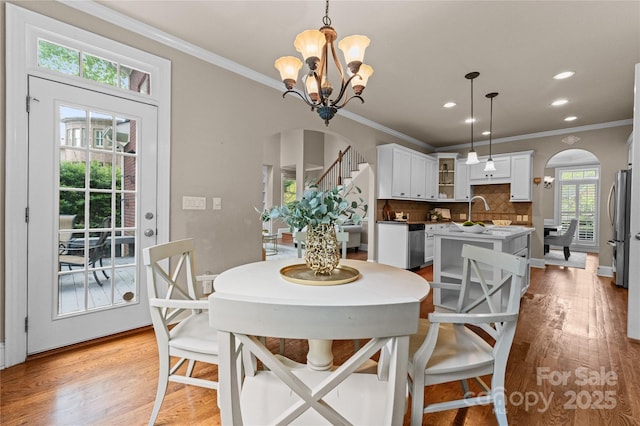 dining room with an inviting chandelier, light wood-style flooring, arched walkways, and ornamental molding