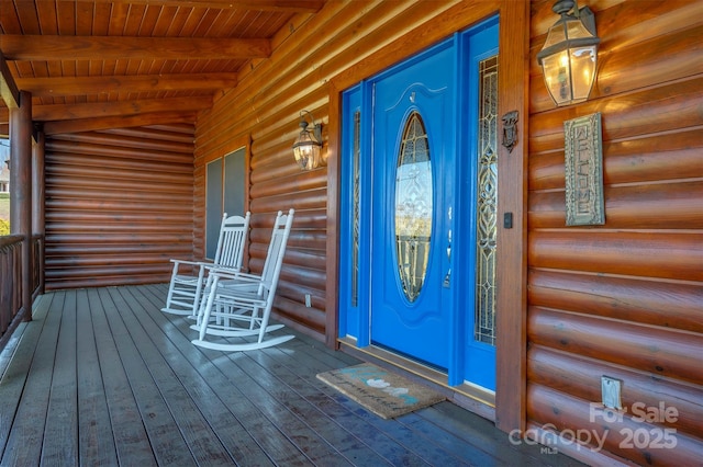 doorway to property with covered porch and faux log siding