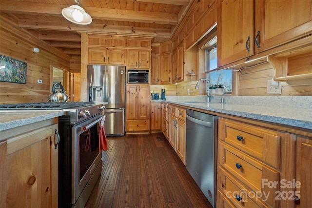 kitchen featuring wooden walls, beam ceiling, appliances with stainless steel finishes, a sink, and wood ceiling