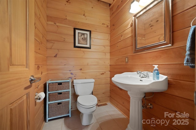 half bathroom with toilet, tile patterned floors, and wooden walls