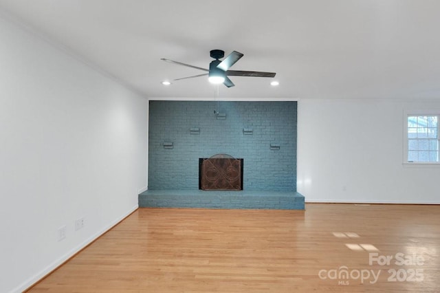unfurnished living room featuring a ceiling fan, a brick fireplace, wood finished floors, and baseboards