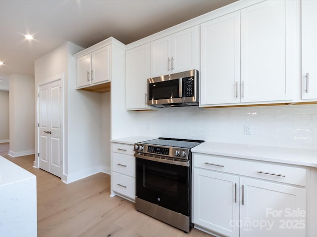 kitchen featuring baseboards, backsplash, light wood-style floors, and appliances with stainless steel finishes