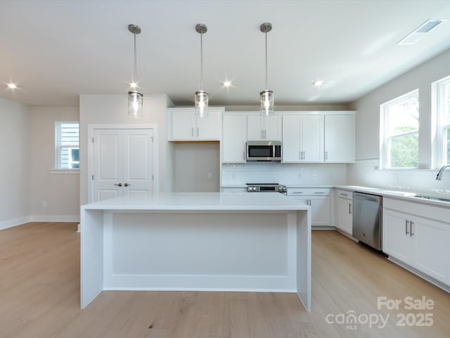 kitchen with stainless steel appliances, visible vents, light wood-style floors, tasteful backsplash, and white cabinetry