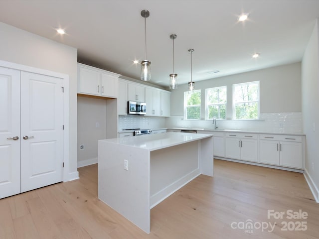 kitchen with stainless steel microwave, backsplash, a sink, and light wood-style flooring