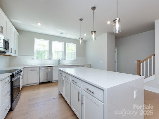 kitchen with light wood-style flooring, a kitchen island, appliances with stainless steel finishes, and a sink