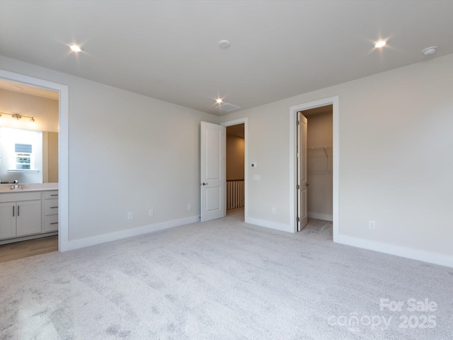 unfurnished bedroom featuring light colored carpet, baseboards, a sink, and a spacious closet