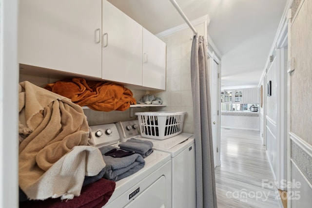washroom with washer and clothes dryer, crown molding, tile walls, light wood-type flooring, and cabinet space