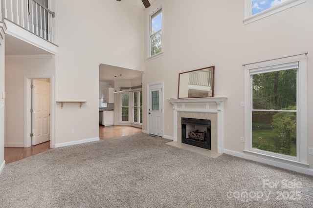 unfurnished living room featuring a towering ceiling, a tile fireplace, a ceiling fan, carpet, and a wealth of natural light