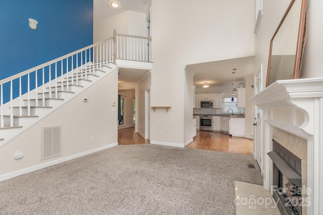 unfurnished living room with visible vents, a fireplace with flush hearth, a high ceiling, light carpet, and stairs