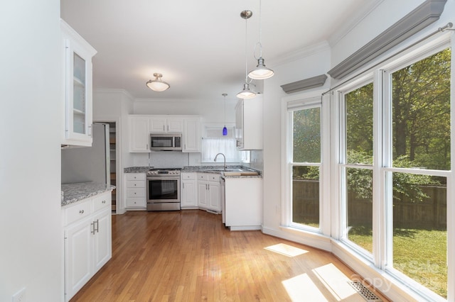 kitchen with appliances with stainless steel finishes, a sink, light wood finished floors, white cabinetry, and glass insert cabinets