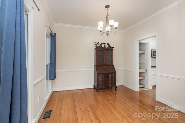unfurnished dining area with crown molding, an inviting chandelier, baseboards, wood finished floors, and visible vents