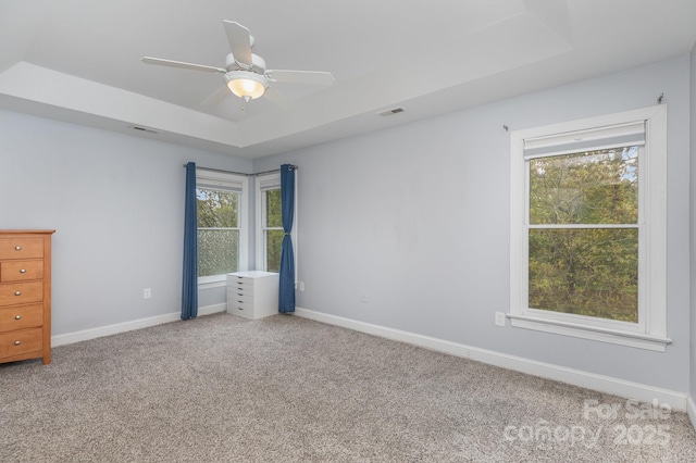 carpeted spare room featuring ceiling fan, visible vents, baseboards, and a raised ceiling