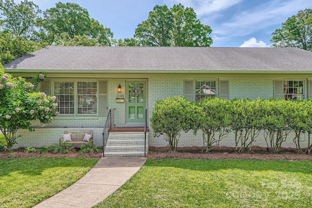 ranch-style house featuring roof with shingles, a porch, and a front yard