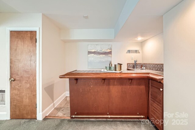 bar featuring indoor wet bar, baseboards, a sink, and carpet flooring