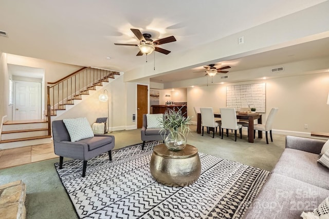 living room featuring carpet, visible vents, stairs, and ceiling fan