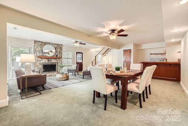 carpeted dining room with visible vents, baseboards, a ceiling fan, stairway, and a fireplace