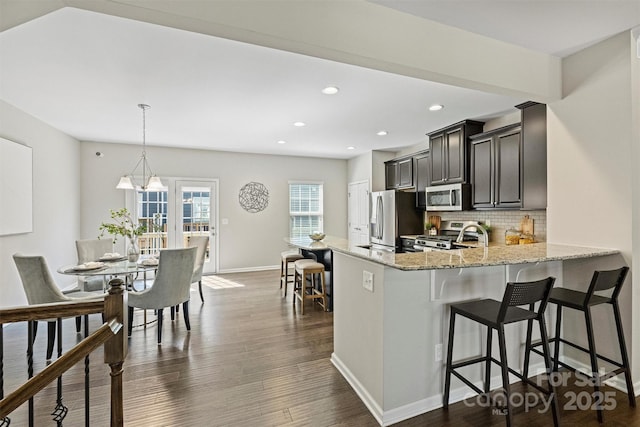 kitchen with light stone counters, a kitchen breakfast bar, dark wood finished floors, appliances with stainless steel finishes, and decorative backsplash