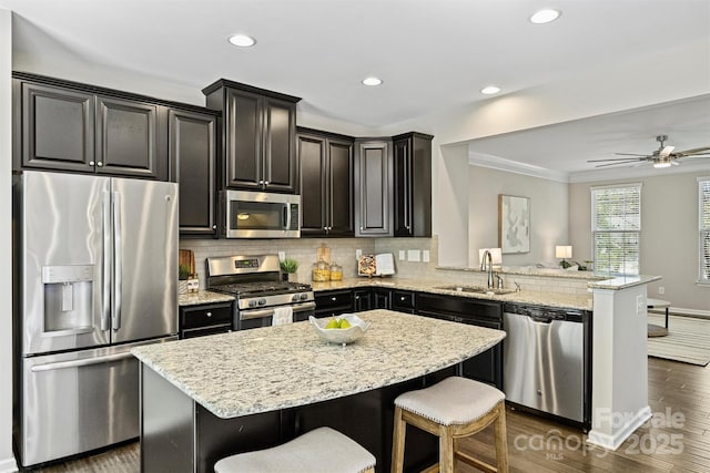 kitchen with a sink, stainless steel appliances, a peninsula, decorative backsplash, and light stone countertops