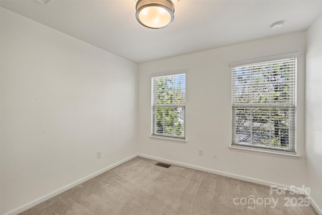 empty room featuring visible vents, light colored carpet, and baseboards