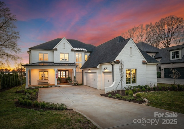 view of front of home with driveway, a porch, metal roof, brick siding, and a standing seam roof