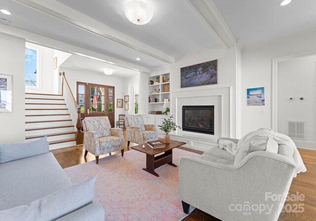living area with beamed ceiling, a glass covered fireplace, visible vents, and recessed lighting