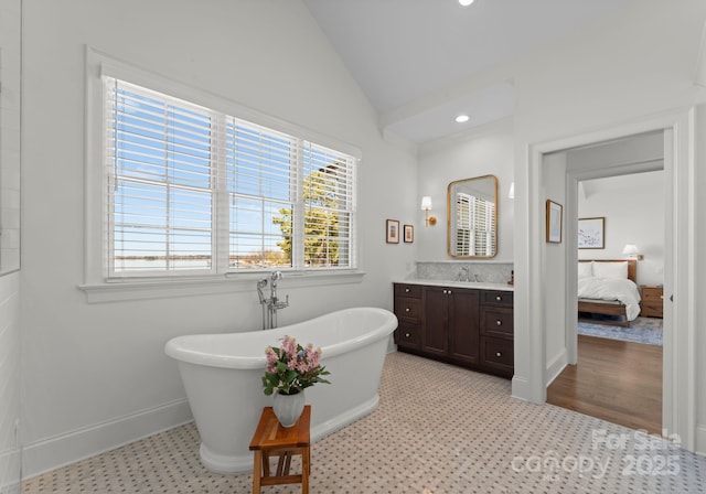 ensuite bathroom with a soaking tub, a healthy amount of sunlight, lofted ceiling, and vanity
