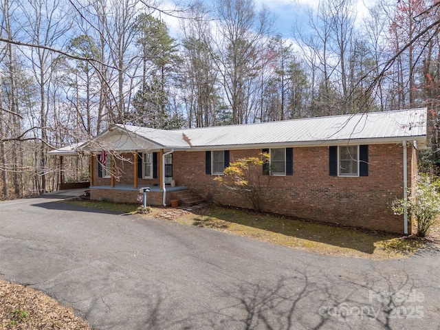 view of front of house featuring brick siding, an attached carport, aphalt driveway, a porch, and metal roof