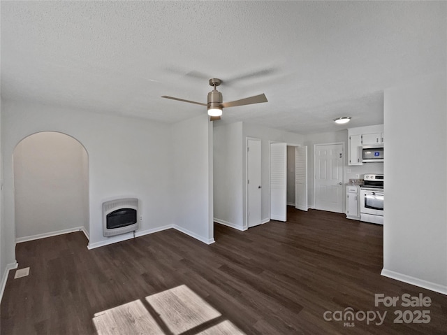 unfurnished living room featuring heating unit, a textured ceiling, dark wood finished floors, baseboards, and ceiling fan