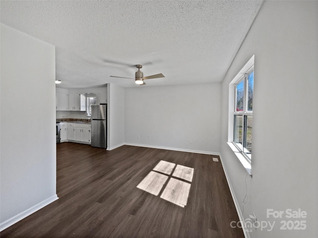 unfurnished living room with a textured ceiling, baseboards, dark wood-style flooring, and ceiling fan