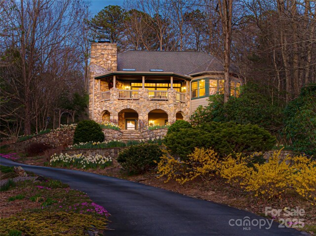 view of front of property featuring stone siding, a balcony, roof with shingles, and a chimney