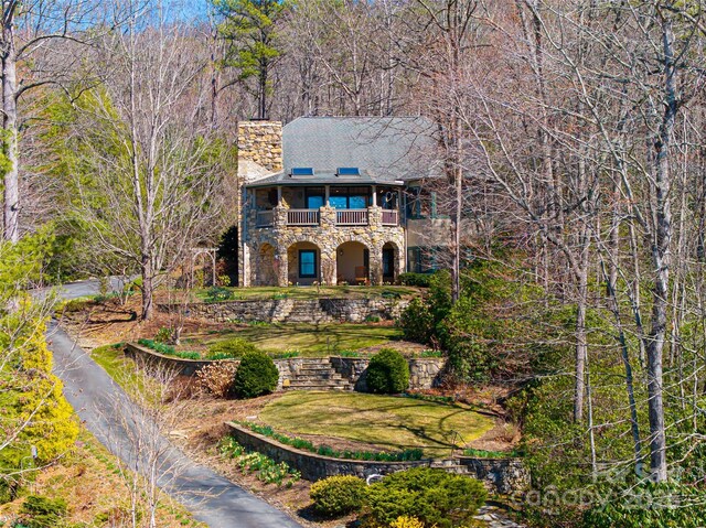 view of front of home with stone siding, a chimney, a front lawn, and a balcony