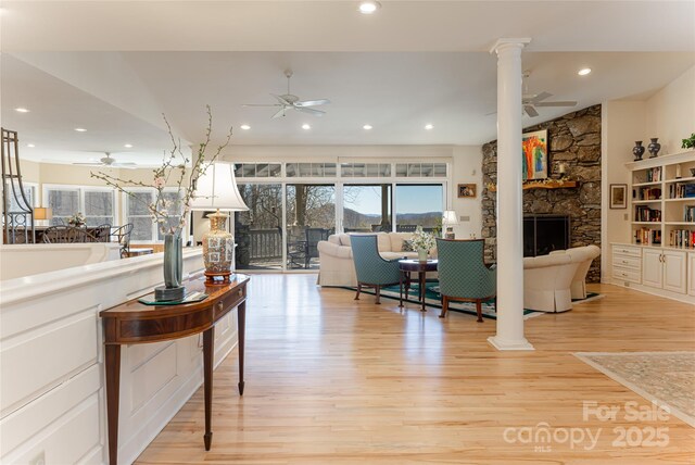 living area featuring ornate columns, light wood-type flooring, and a ceiling fan