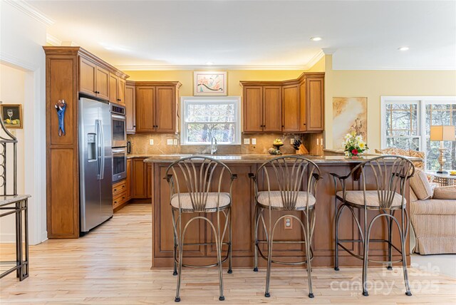 kitchen featuring a breakfast bar area, appliances with stainless steel finishes, brown cabinetry, and light wood finished floors