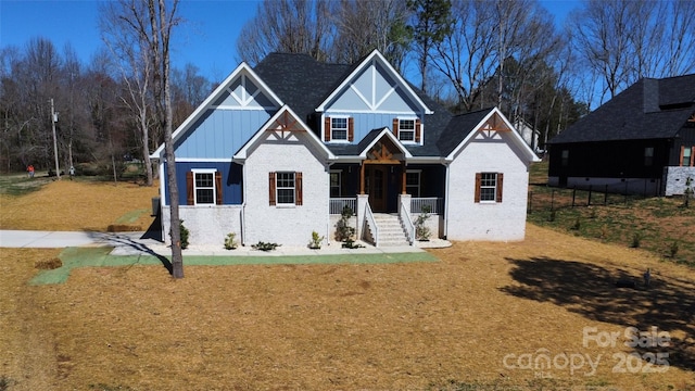 view of front of home featuring board and batten siding, a front lawn, covered porch, and brick siding