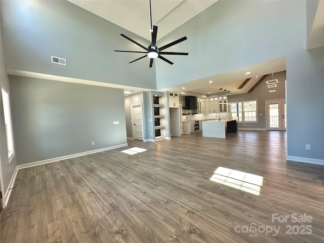 unfurnished living room featuring visible vents, baseboards, wood finished floors, a ceiling fan, and a sink