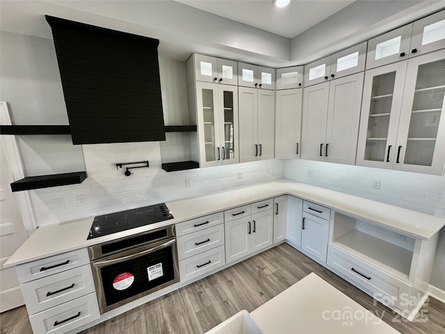 kitchen featuring stainless steel oven, black electric cooktop, light wood-style floors, and white cabinets