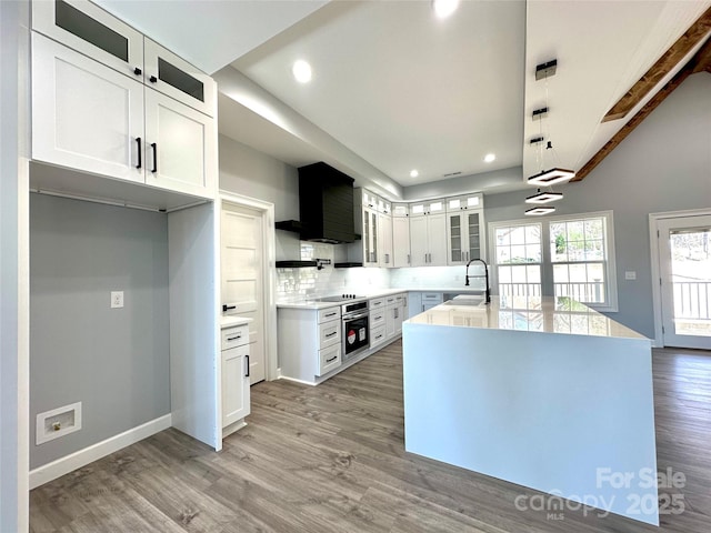 kitchen featuring glass insert cabinets, stainless steel oven, light wood-style floors, white cabinets, and a sink