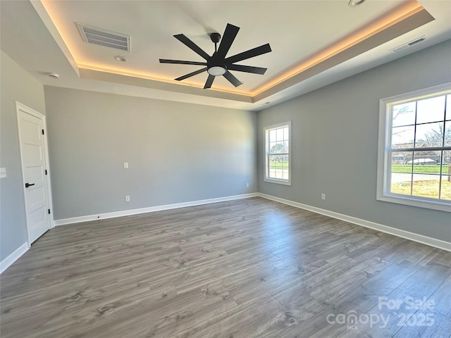 unfurnished room with visible vents, a ceiling fan, a tray ceiling, wood finished floors, and baseboards