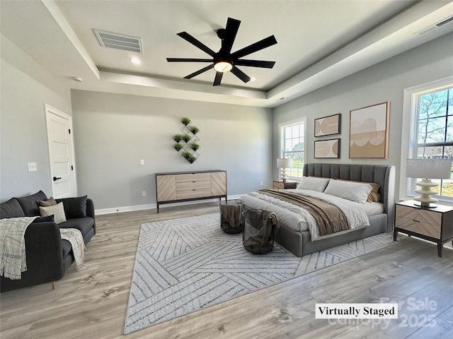 bedroom with visible vents, light wood-type flooring, a raised ceiling, and baseboards