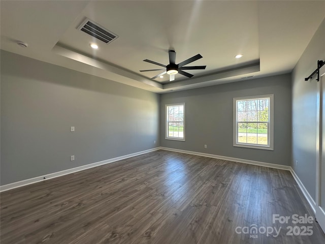 unfurnished room featuring visible vents, dark wood finished floors, baseboards, a barn door, and a raised ceiling