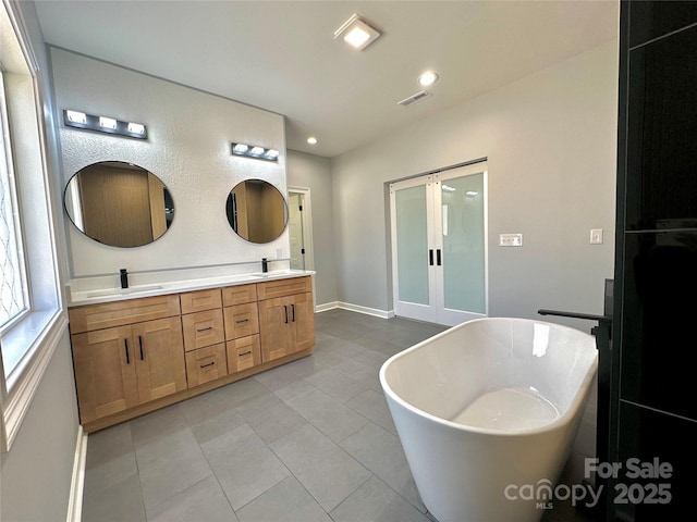 bathroom featuring double vanity, a freestanding tub, visible vents, and a sink