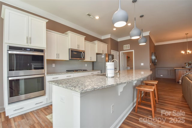 1638 Sweetmoss Loop, Denver, NC 28037 - kitchen with stainless steel appliances, light wood finished floors, a breakfast bar, white cabinetry, and ornamental molding