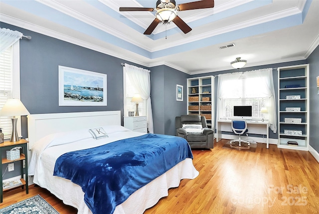 bedroom with wood finished floors, a tray ceiling, visible vents, ceiling fan, and ornamental molding