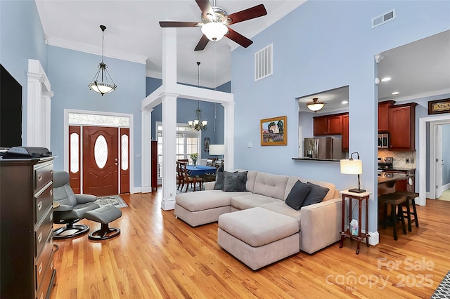 living room with light wood finished floors, visible vents, ornate columns, and a towering ceiling