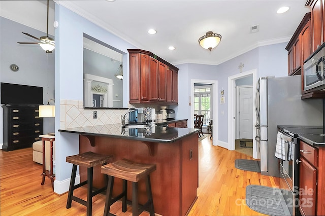 kitchen featuring light wood finished floors, decorative backsplash, a ceiling fan, dark countertops, and appliances with stainless steel finishes